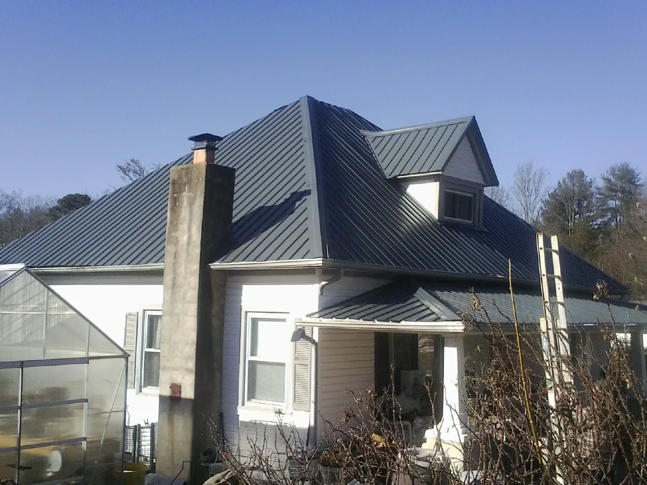 Dark blue standing seam metal roof on a white farmhouse with dormer — Slate & Tile Roof Repair by Roofing Brothers in Bowie