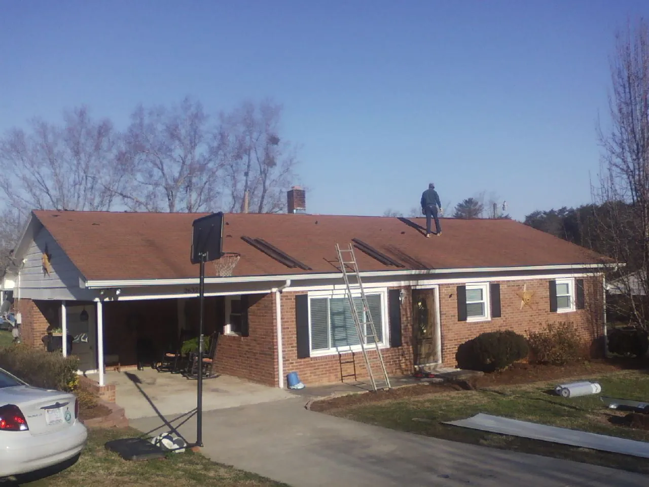 Roofer stripping a shingle roof on a brick ranch before metal panels in Bowie