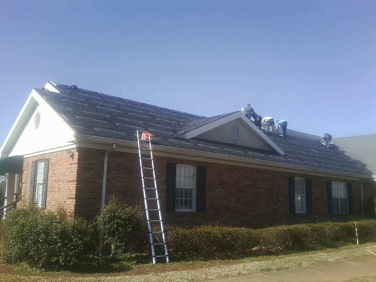 Crew tearing shingles off a brick ranch roof with a ladder set — Metal Roof Repair work by our crew in Bowie