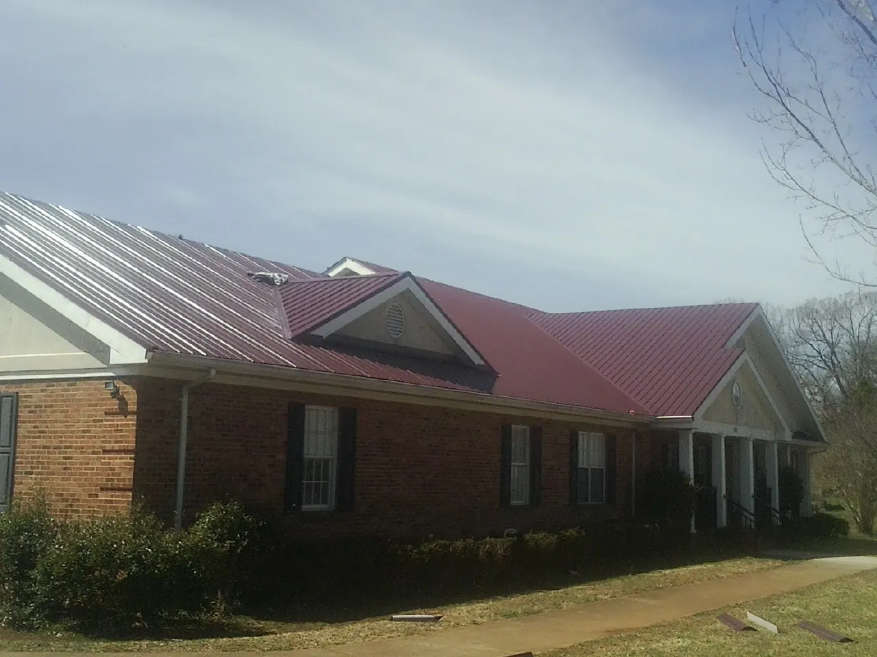 Red metal roof with gabled entries on a long brick building, from a Hail Damage Roof Repair job in Bowie