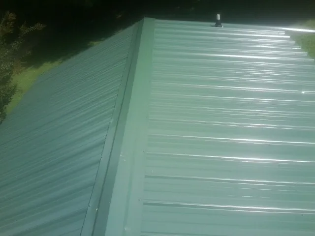 New green metal panels meeting at the ridge of a roof — Flat Roof Repair work by our crew in Bowie