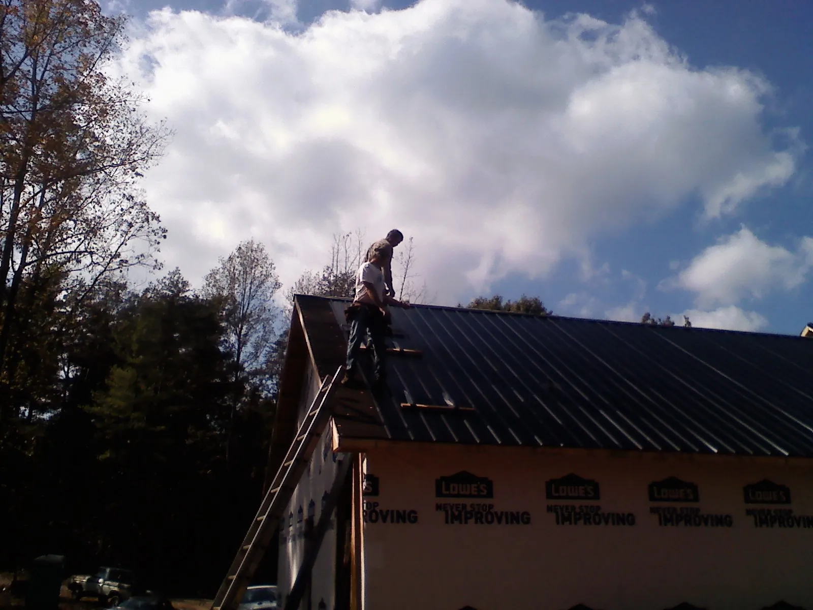 Roofer fastening dark metal panels high against a cloudy sky, from a Roof Inspection job in Bowie