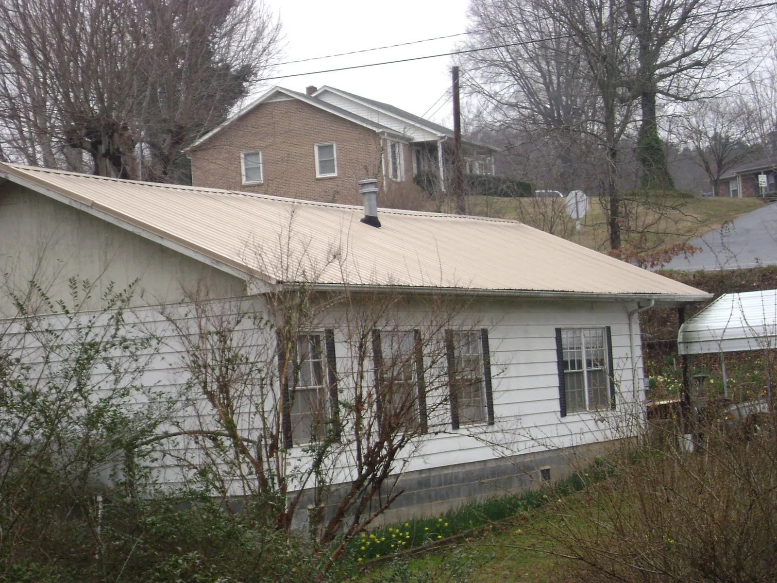 Tan metal roof on a white sided house set into a hillside — Commercial Roofing by Roofing Brothers in Bowie